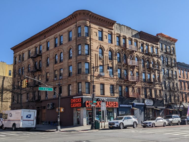 A brick corner apartment building at First Avenue in East Harlem, February 2022