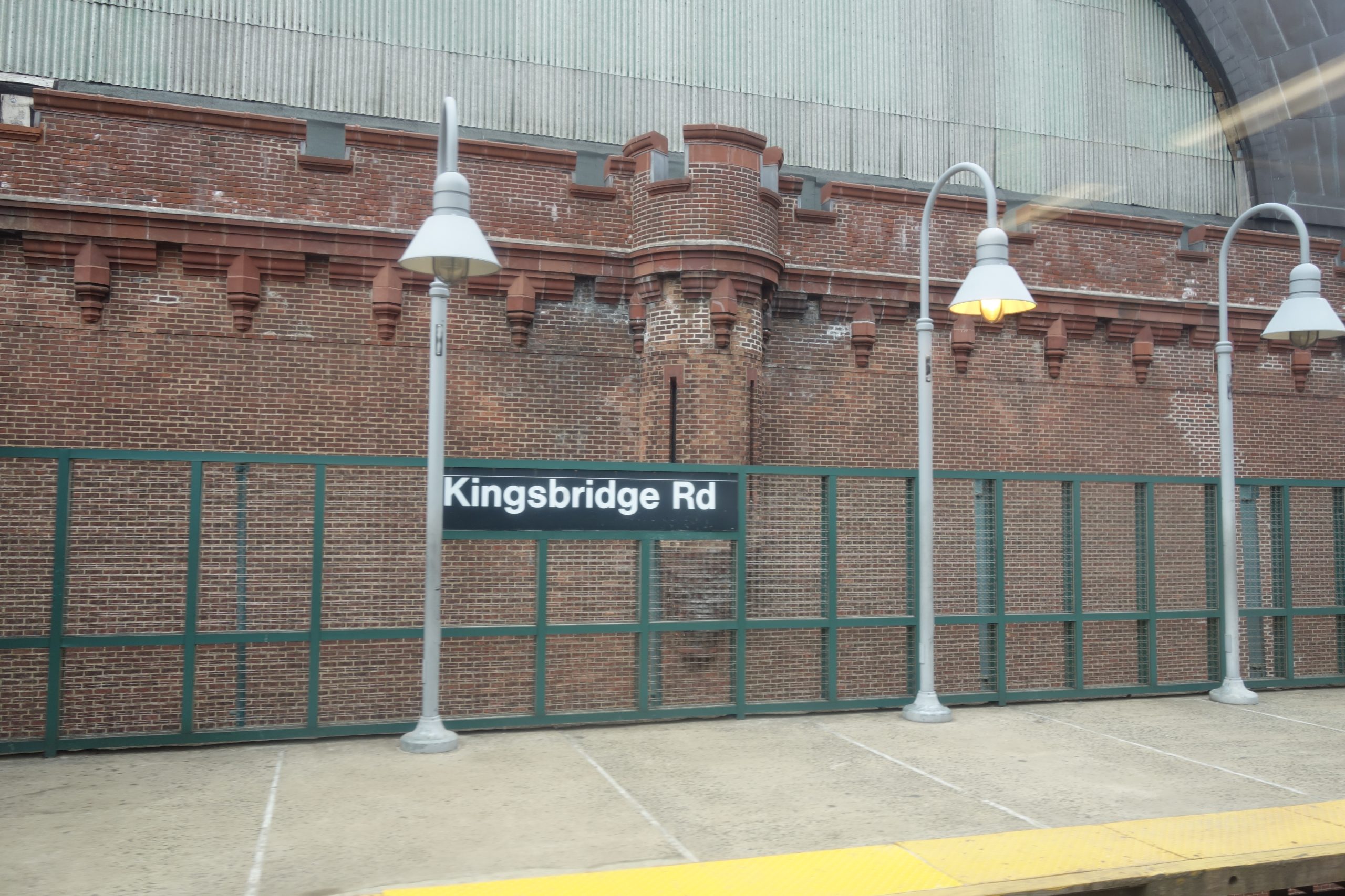 The Kingsbridge Road station on the 4 line, with the brick wall of the Kingsbridge Armory behind it
