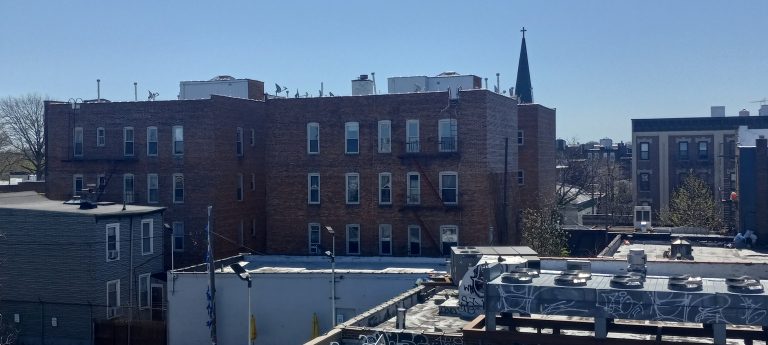 Brick apartment buildings and a church spire across Ridgewood's rooftops